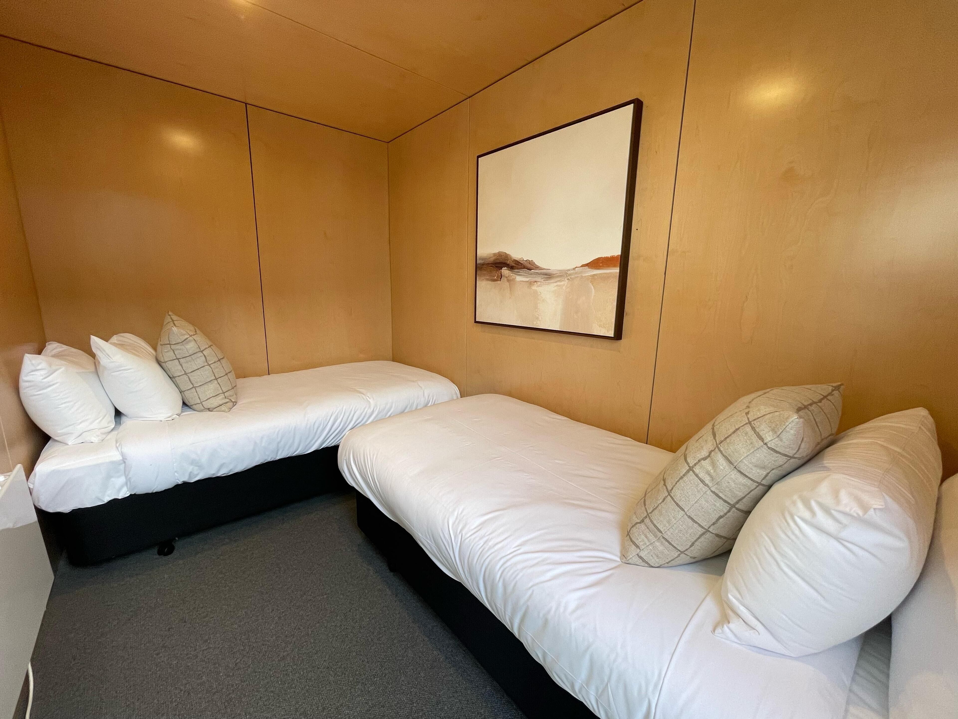 A hotel room with two beds, a gray carpet, and a painting on the wall.