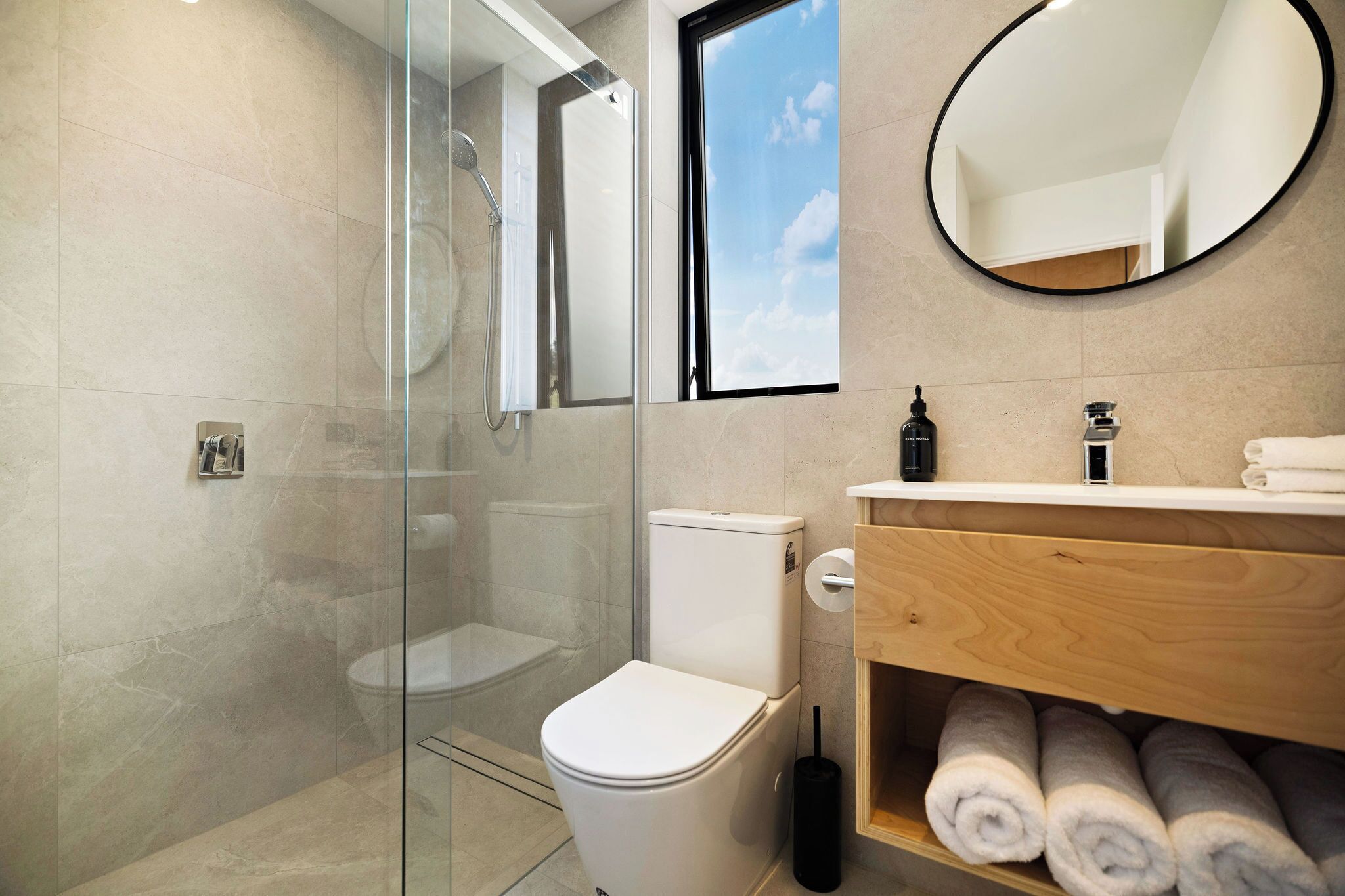 Un baño moderno con cabina de ducha de vidrio, inodoro blanco y tocador de madera con toallas.
