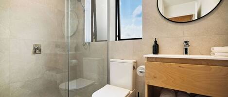 Ein modernes Badezimmer mit Duschkabine aus Glas, einer weißen Toilette und einem Holzbadezimmer-Möbel mit Handtüchern.