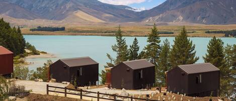 A rustic cabin area with three cabins overlooking a turquoise lake, surrounded by mountains and pine trees.