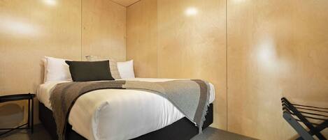 Ein modernes Schlafzimmer mit einem hölzernen Kopfteil, einem Bett mit weißen Bettbezügen, einer grauen Tagesdecke und einem schwarzen Kissen.