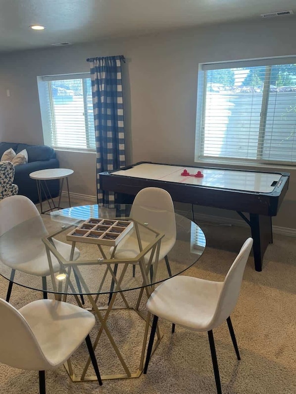 Una sala de estar con mesa de billar, sofá azul, una pequeña mesa redonda y una mesa de centro de vidrio con sillas.