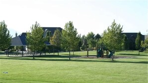 Ein Park mit einem Spielplatz, Bäumen und einem Gebäude im Hintergrund.
