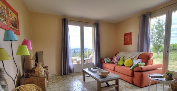 A living room with a sofa, a coffee table, a lamp, and a view through a glass door. - La Treille - FRONTENAS (FRONTENAS)