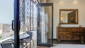 A balcony with a glass door, a dining table with chairs, a wooden dresser with a mirror, and a view of the cityscape.