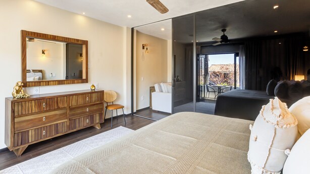 A modern bedroom with a large bed, a wooden dresser, a mirror, and a ceiling fan.
