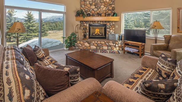 A cozy living room with a stone fireplace, comfortable seating, and a large window offering a scenic view.