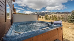 A hot tub with a wooden exterior, set against a backdrop of mountains and a clear sky.