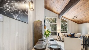 Un comedor con mesa de madera dispuesta para cuatro, un sofá blanco y un ventanal con vistas a árboles.