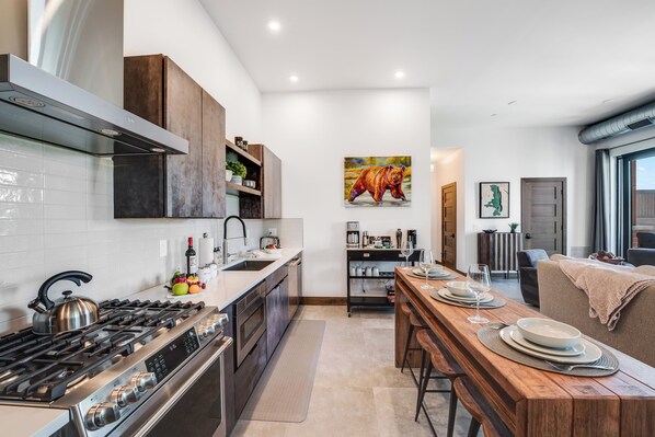 A modern kitchen with a gas stove, stainless steel appliances, and a wooden dining table set for four. - Located in Downtown Whitefish,Walk to Dining and Shops- Nearby Lake and Ski! (Whitefish)