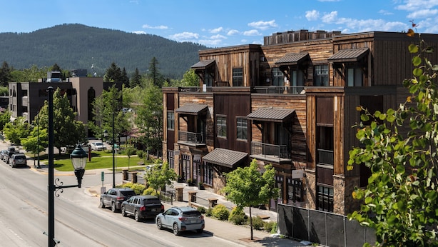 A multi-story building with a rustic wooden facade, multiple balconies, and a street view with parked cars and a clear sky. - Located in Downtown Whitefish,Walk to Dining and Shops- Nearby Lake and Ski! (Whitefish)