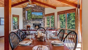 Une salle à manger avec une cheminée en pierre, de grandes fenêtres et un plafond en bois.