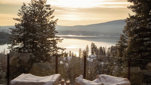 Une scène hivernale avec un lac, des arbres couverts de neige, et une chaise sur laquelle est posée une couverture et une tasse.
