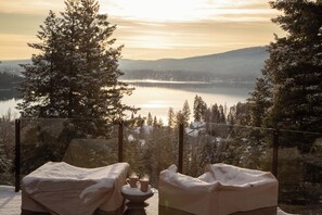 Une scène hivernale avec un lac, des arbres couverts de neige, et une chaise sur laquelle est posée une couverture et une tasse.