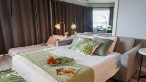 A hotel room with a large bed, two armchairs, a small table, and a window with curtains.