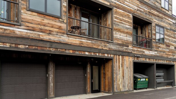 A multi-story building with a rustic wooden facade, large windows, and a garage with a green dumpster. - Loft in heart of Downtown- Walk to City Beach, Dining & Shops! Modern Loft (Whitefish)