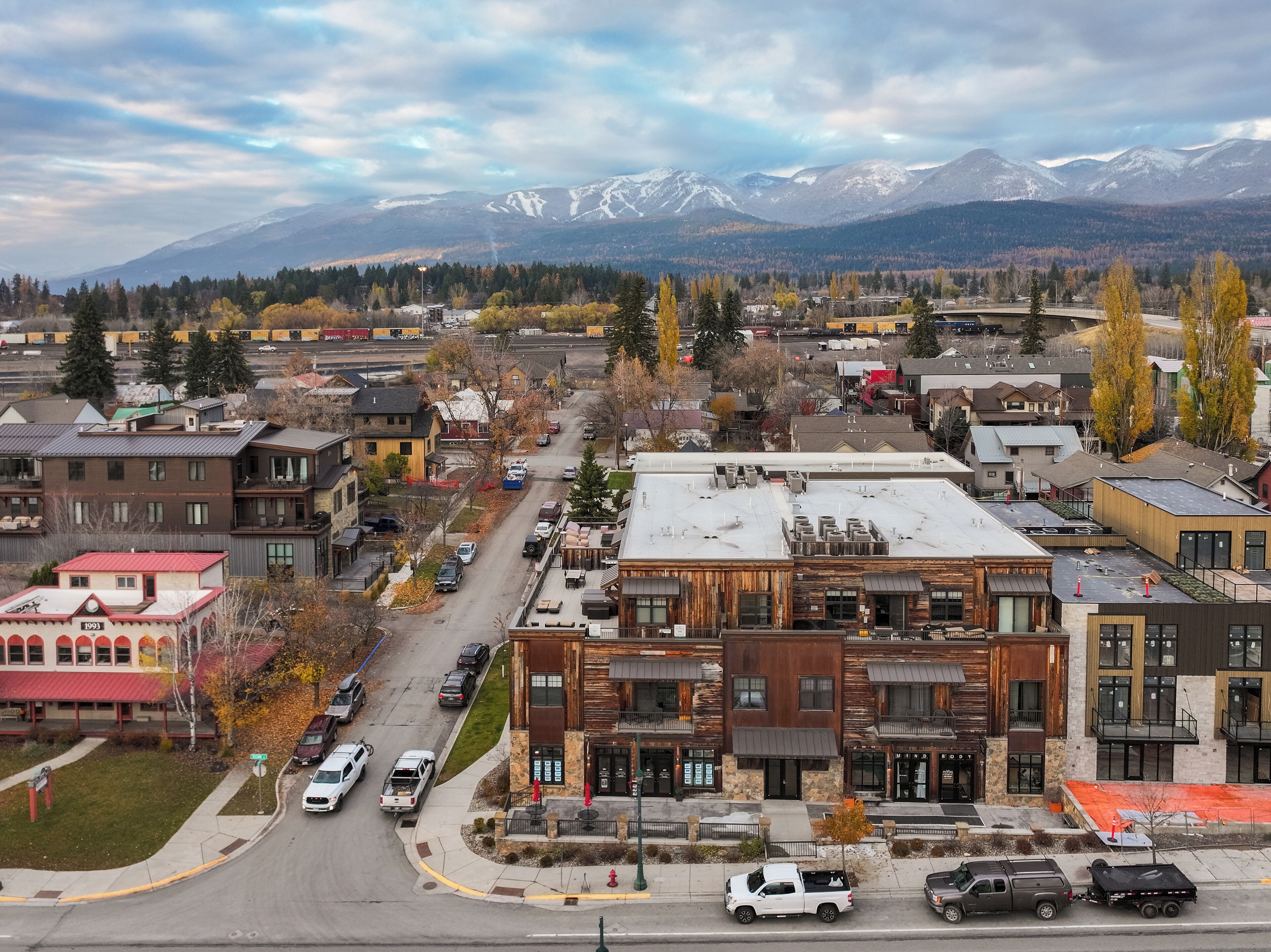 A town with a mix of modern and traditional buildings, a main street with parked cars, and mountains in the background.