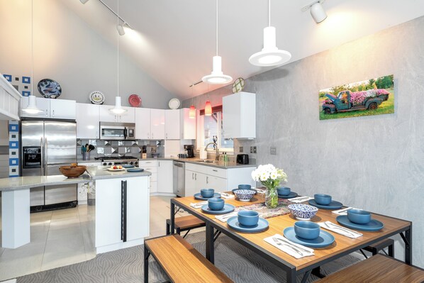 A modern kitchen with white cabinets, stainless steel appliances, and a dining area set with blue plates and bowls.