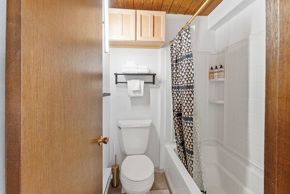 Un baño pequeño y funcional con inodoro, un estante con toallas dobladas y cortina de ducha.