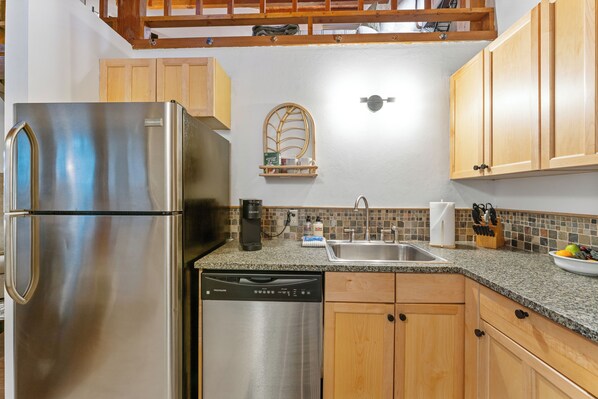 Una cocina con electrodomésticos de acero inoxidable, gabinetes de madera, encimera de granito y lavavajillas integrado.