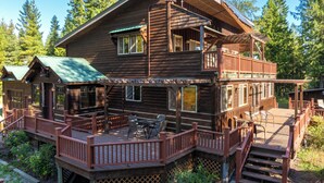 Eine zweistöckige Blockhütte mit einer Terrasse, Sitzgelegenheiten im Freien und einer Treppe, die zum oberen Stockwerk führt.