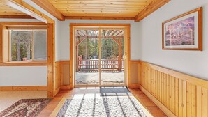 Ein Holzinterieur mit einer großen Schiebeglasdoor, die auf eine Terrassenfläche führt, einem gerahmten Gemälde an der Wand und einem strukturierten Teppich auf dem Boden.