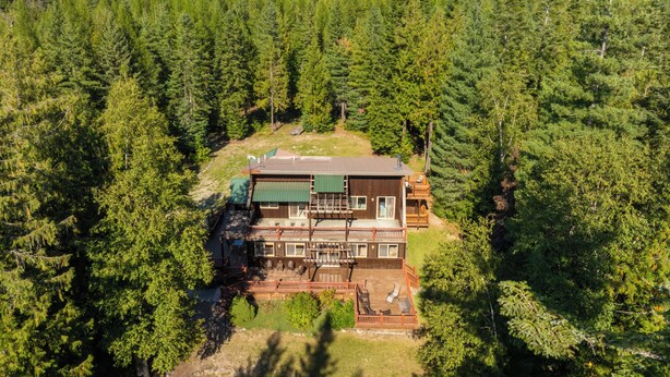 Eine zweigeschossige Holzhütte mit einer Terrasse und Sitzbereich im Freien, umgeben von dichtem Wald.