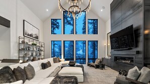 A modern living room with a large sofa, a fireplace, and a large window with a view of trees.