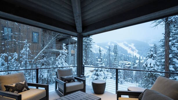 A cozy balcony with a view of snow-covered trees and mountains.