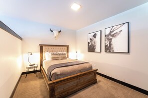 Une chambre à coucher avec un lit en bois, une tête de lit, deux lampes de chevet et un crâne de taureau fixé au mur.