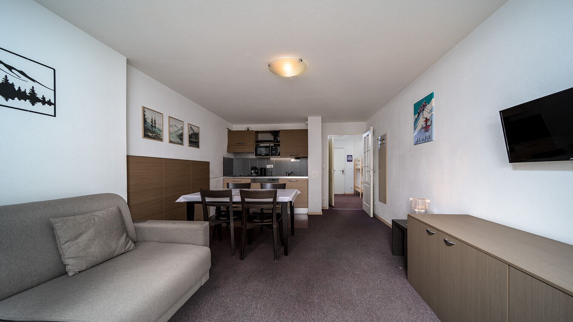Une chambre d’hôtel compacte comprenant un canapé, une table à manger avec des chaises, un coin cuisine, un téléviseur fixé au mur et un petit meuble de rangement.