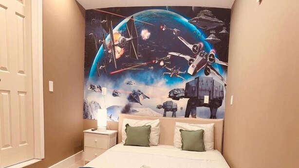 A bedroom with a bed, pillows, a nightstand, and a wall mural of space-themed artwork. - Atrium Design District (Miami)