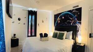 A bedroom with a large bed, a nightstand with a lamp, a wall with space-themed decorations, and a window with curtains. - Atrium Design District (Miami)
