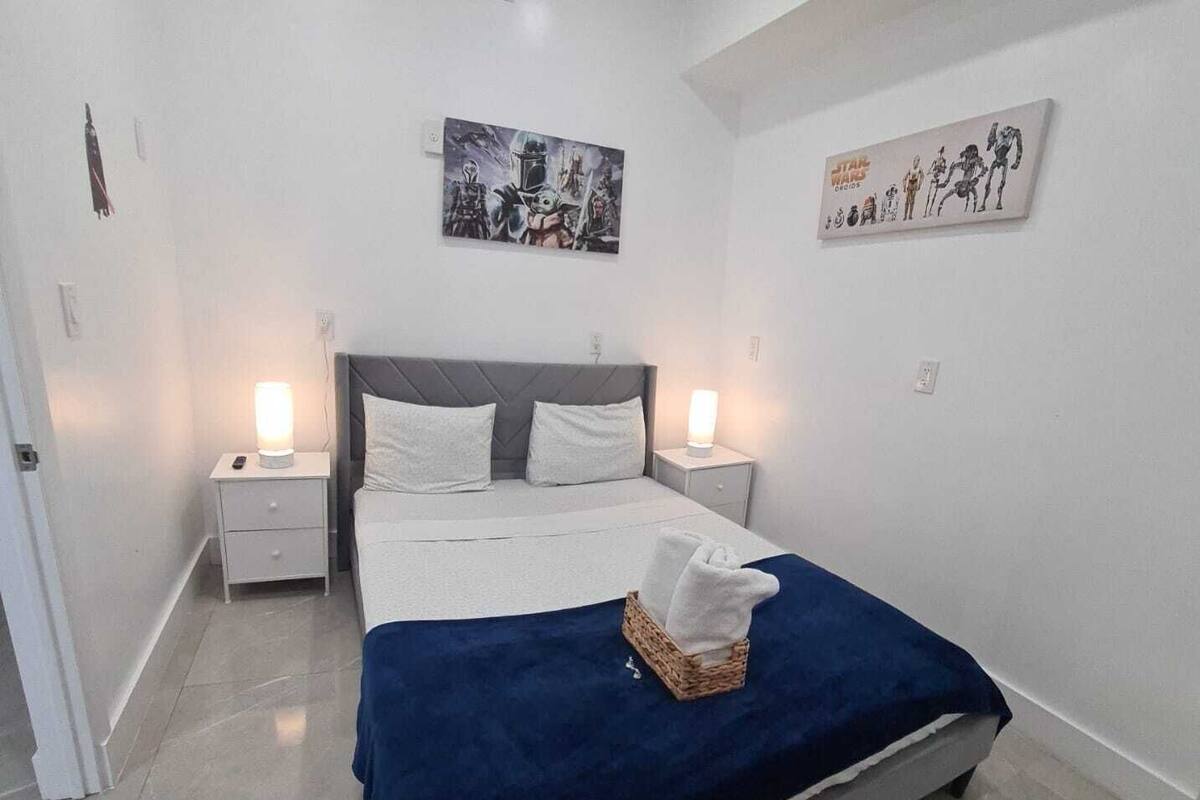 Quarto com cama, duas mesas de cabeceira, um criado-mudo, obra de arte na parede e abajur.