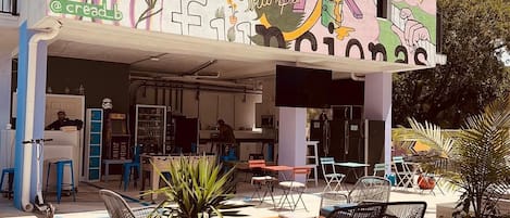 Een kleurrijk gebouw met een muurschildering, terras en een bar.