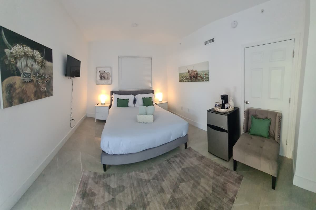 Quarto com cama, mesas de cabeceira, cafeteira, cadeira e obras de arte nas paredes.