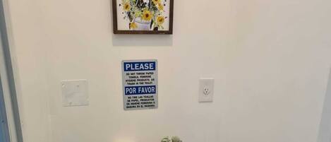 A small, narrow bathroom with a toilet, a trash bin, and a framed picture above the toilet.