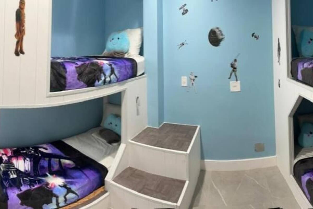 Quarto com beliches, escada e decorações nas paredes, incluindo temas espaciais.