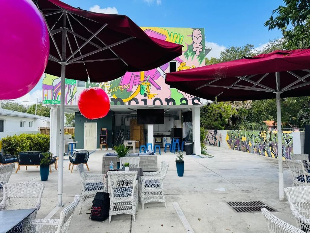 An outdoor seating area with wicker chairs and tables, a mural on the building, and a red balloon.