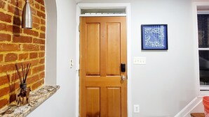 Un pasillo con puerta de madera, pared de ladrillo, lámpara colgante y un cuadro enmarcado.