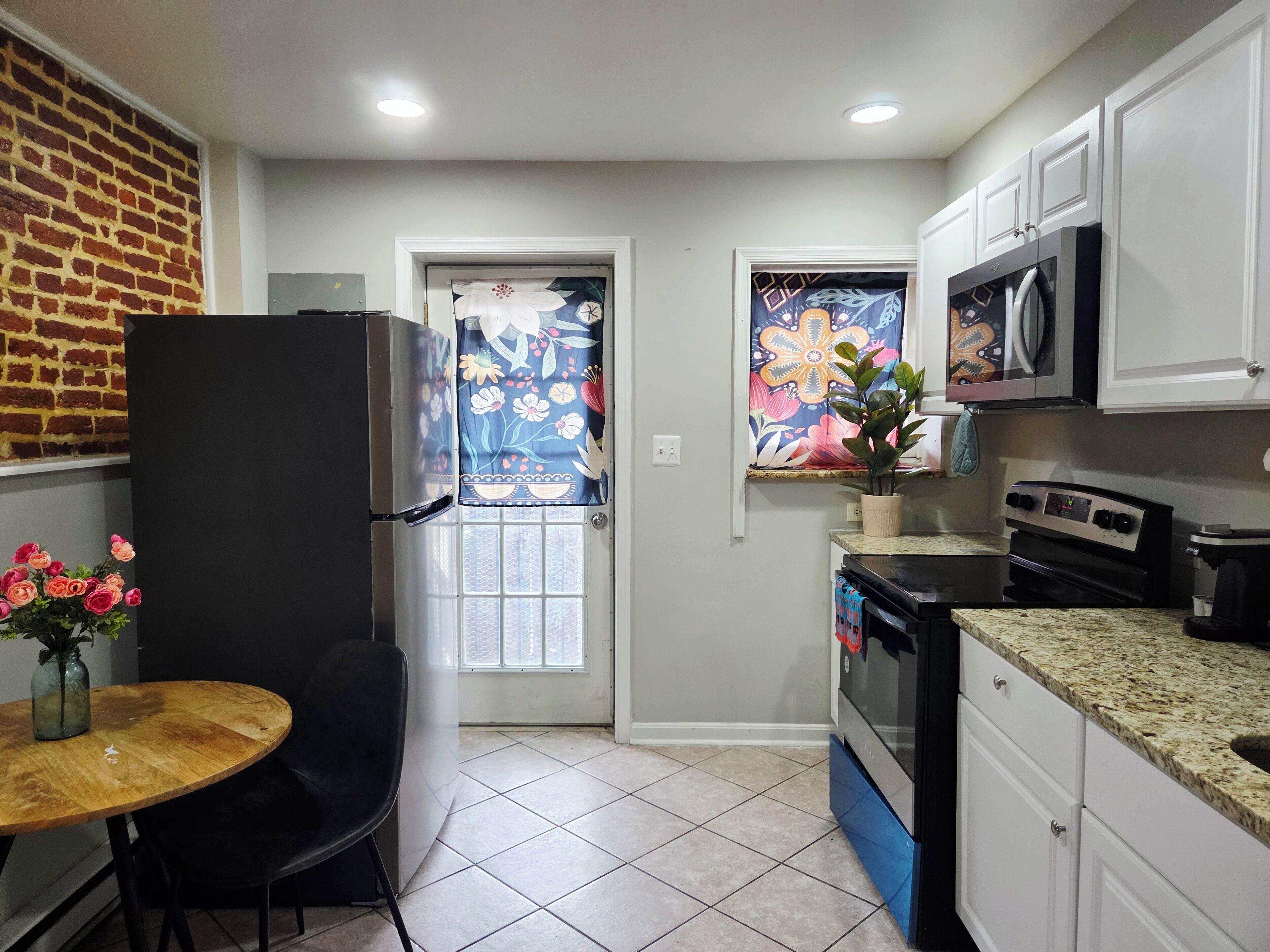 Una cocina con refrigerador, estufa, microondas y una ventana con cortina estampada.
