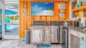 A kitchen with a stone backsplash, stainless steel appliances, wooden paneling, and a large painting of a beach scene.