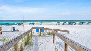 Une plage avec des allées en bois, des rangées de chaises de plage bleues et des parasols.