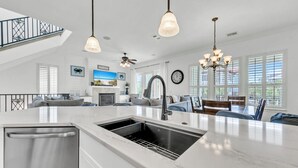 Une cuisine moderne dotée d’un grand îlot central, d’appareils électroménagers en acier inoxydable et de luminaires suspendus.