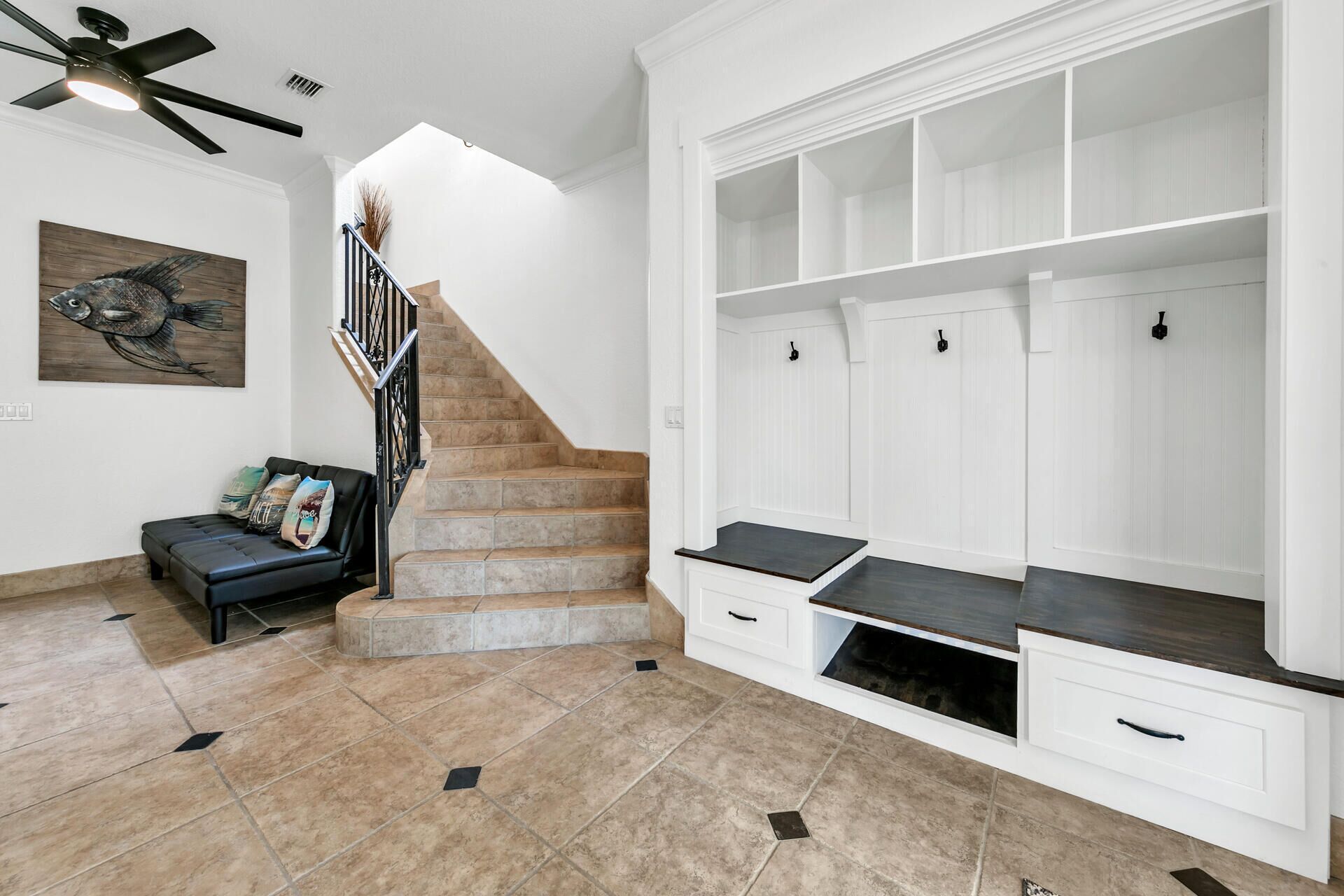 A spacious living area with a staircase, a black leather sofa, a fish painting, and a built-in entertainment unit with shelves and drawers.