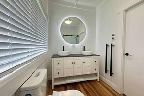 A bathroom with a white vanity, two sinks, a mirror, and a toilet. - Miami one one - Ultimate 3 Bedroom - Walk to Beach, Village and 2 Vineyards (Waiheke Island)