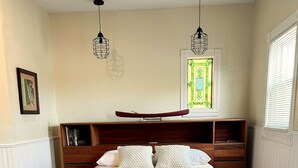 Une chambre à coucher avec un grand lit, une tête de lit en bois, des tables de chevet, une commode en bois et une fenêtre à vitraux.