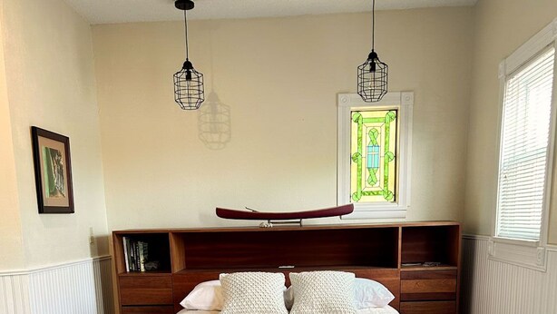 A bedroom with a large bed, wooden headboard, bedside tables, a wooden dresser, and a stained glass window. - Great Water Inn (Bayfield)