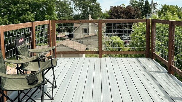Une terrasse en bois avec une rambarde en métal, une table et deux chaises.
