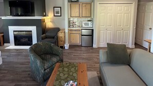 A living room with a fireplace, a television, a sofa, and a coffee table. - Wraparound Deck - 208B (Kelowna)